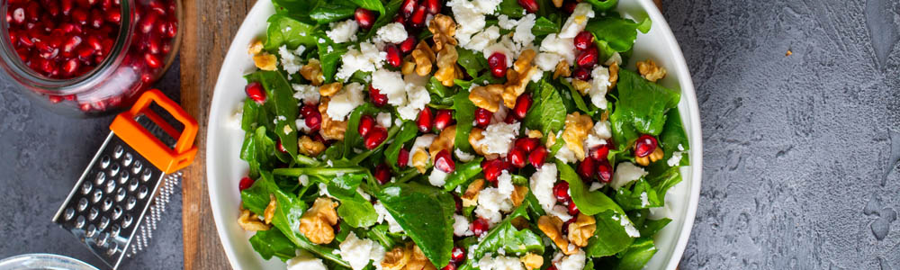 Close-up of pomegranate salad featuring nuts and cheese on a bed of greens